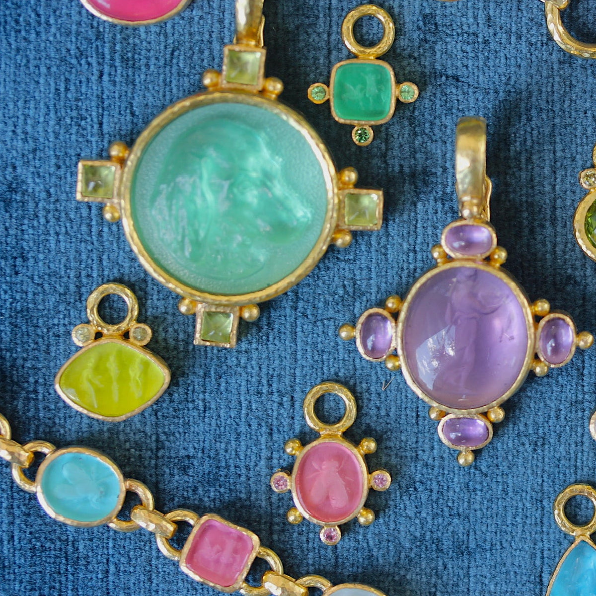 Colorful gemstone pendants on gold chains against a blue fabric background
